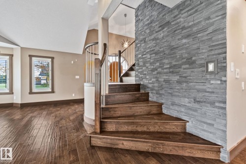 Wood-finish flooring throughout, curved staircase with wood treads and white balusters, stacked stone accent wall, and multiple windows with plantation shutters - 10 Eldorado Drive, St. Albert, AB 
