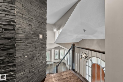 Stacked stone accent wall, wood-finish flooring, metal balusters with wood handrail, recessed lighting, and a decorative pendant light fixture - 10 Eldorado Drive, St. Albert, AB 