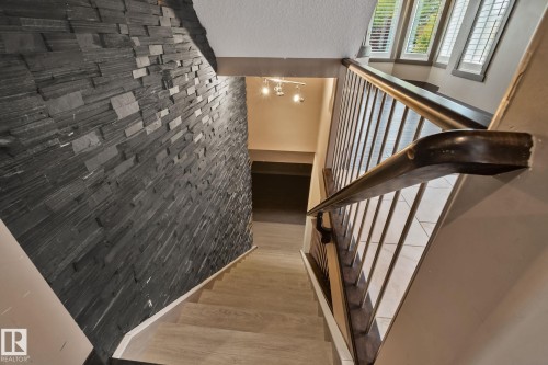 Staircase featuring wood-finish treads, a decorative dark wood handrail, metal balusters, and a textured dark stone accent wall - 10 Eldorado Drive, St. Albert, AB 