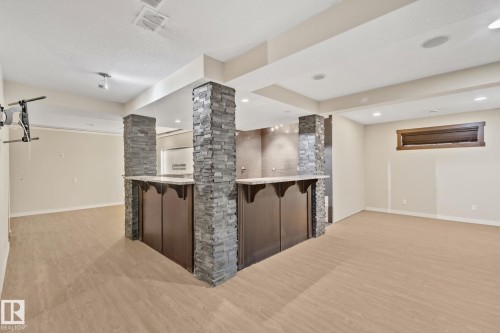 Spacious lower level featuring wood-finish flooring, recessed lighting, and a built-in bar with stone-clad columns and a light-toned countertop - 10 Eldorado Drive, St. Albert, AB 