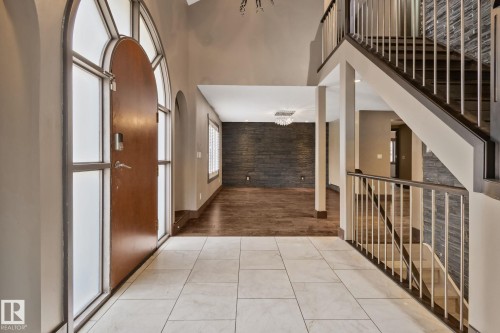 Arched wood-finish entry door with frosted glass sidelights, tile flooring, two-story foyer, wood-finish flooring, and a staircase with white balusters - 10 Eldorado Drive, St. Albert, AB 