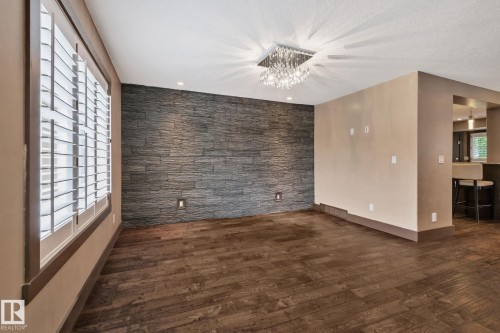 Wood-finish flooring, accent wall with stacked stone, crystal chandelier, and plantation shutters - 10 Eldorado Drive, St. Albert, AB 
