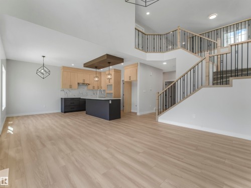 Open-concept living area with wood-finish flooring, a contemporary kitchen featuring a large island, two-tone cabinetry, and a full backsplash - 11 Dalquist Bay, Leduc, AB 