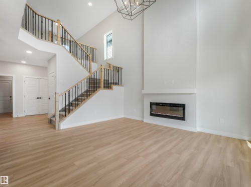 Soaring ceilings, a grand staircase with wrought iron balusters, wood-finish flooring, a contemporary electric fireplace, and recessed lighting - 11 Dalquist Bay, Leduc, AB 