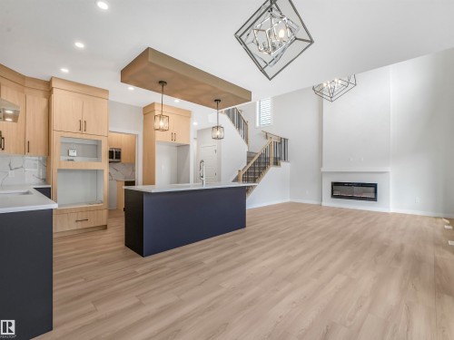 Open-concept living area featuring wood-finish flooring, a contemporary linear fireplace, and a kitchen island with pendant lighting - 11 Dalquist Bay, Leduc, AB 
