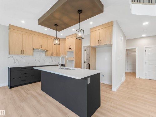 Modern kitchen featuring light wood-finish cabinetry, a dark gray kitchen island, white countertops, a patterned backsplash, and recessed lighting - 11 Dalquist Bay, Leduc, AB 