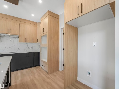 Modern kitchen featuring wood-finish upper cabinetry, dark lower cabinetry, and a white countertop island - 11 Dalquist Bay, Leduc, AB 