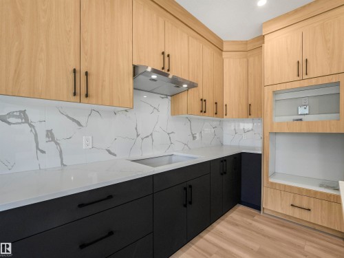 Two-tone cabinetry with wood-finish upper cabinets and dark lower cabinets, white countertops, a tile backsplash with gray veining, and wood-finish flooring - 11 Dalquist Bay, Leduc, AB 