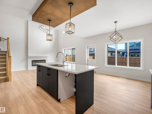 Spacious interior with high ceilings, light wood-finish flooring, a contemporary kitchen island with a white countertop, and modern pendant lighting fixtures - 11 Dalquist Bay, Leduc, AB 