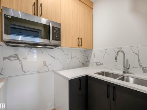 Stainless steel microwave, dual basin undermount sink, chrome gooseneck faucet, light wood-finish upper cabinetry, and dark lower cabinetry with matte black hardware - 11 Dalquist Bay, Leduc, AB 