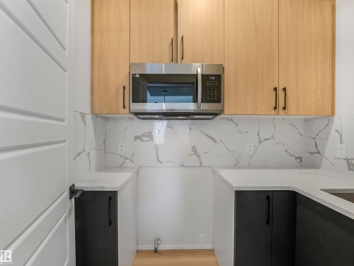 Light wood-finish upper cabinetry, black lower cabinetry, stainless steel microwave, stone-finish countertops, and wood-finish flooring - 11 Dalquist Bay, Leduc, AB 