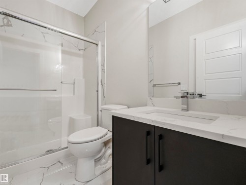 Vanity with a quartz countertop and integrated sink, modern dark cabinetry with matte black hardware, chrome faucet, wall-mounted mirror, and a shower with a sliding glass door - 11 Dalquist Bay, Leduc, AB 