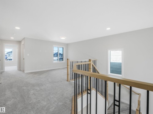 Open concept upper landing featuring light gray carpeting, multiple windows, and a staircase with wood-finish handrails and black metal balusters - 11 Dalquist Bay, Leduc, AB 