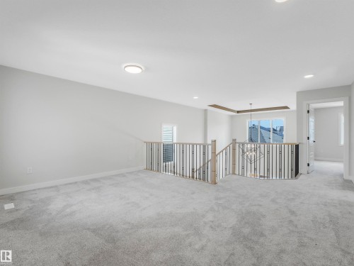 Spacious carpeted landing featuring a wood and metal spindle railing, overhead lighting, and a window with exterior views - 11 Dalquist Bay, Leduc, AB 