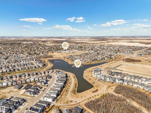 Aerial perspective of a developed neighborhood featuring residential properties, a central lake, and open land areas - 11 Dalquist Bay, Leduc, AB 