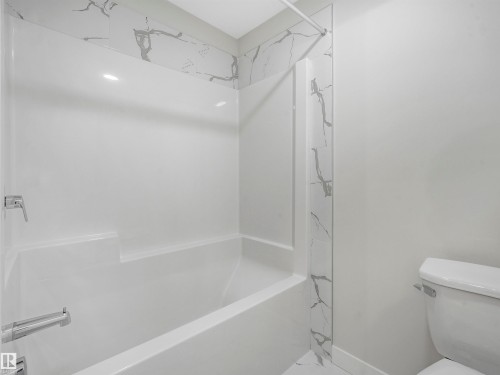 Bathtub with white surround and chrome fixtures, accented by marble-patterned wall panels - 11 Dalquist Bay, Leduc, AB 