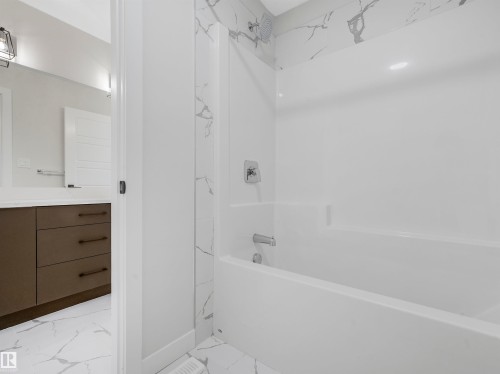 Bathtub with integrated shower, chrome fixtures, and a tiled surround with a marble-look finish - 11 Dalquist Bay, Leduc, AB 