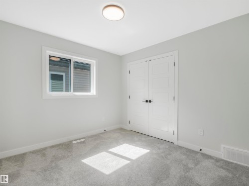Bright secondary bedroom featuring neutral wall finishes, recessed ceiling lighting, dual closets with white panel doors, and a large casement window with exterior views - 11 Dalquist Bay, Leduc, AB 