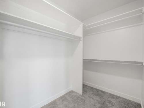 Walk-in closet featuring built-in shelving, hanging rods, and grey carpeting - 11 Dalquist Bay, Leduc, AB 