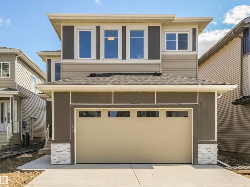 Contemporary exterior featuring a beige garage door, white framed windows, horizontal siding, and decorative stone accents - 11 Dalquist Bay, Leduc, AB 