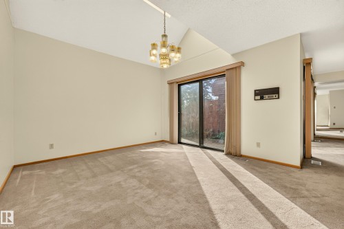 Vaulted ceiling featuring a brass chandelier, neutral carpeting, and a sliding glass door - #23 500 Lessard Dr Nw, Edmonton, AB 