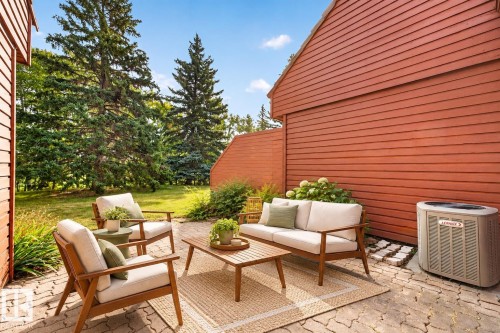 Paved patio area, natural wood-tone exterior siding, landscaped shrubbery, and mature evergreen trees - #23 500 Lessard Dr Nw, Edmonton, AB 