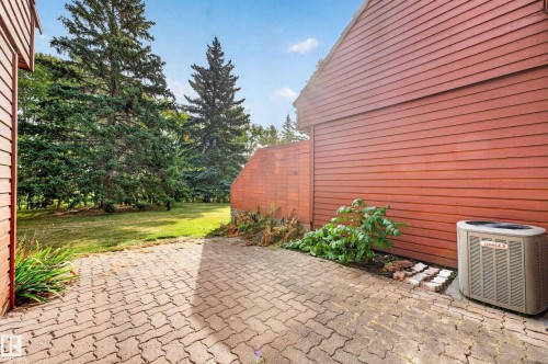Expansive outdoor paving stone area with a surrounding lawn and mature trees - #23 500 Lessard Dr Nw, Edmonton, AB 