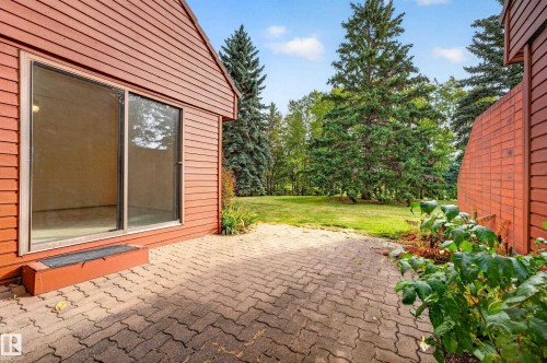 Exterior siding with horizontal panels, sliding glass door, paved patio, and mature evergreen trees - #23 500 Lessard Dr Nw, Edmonton, AB 