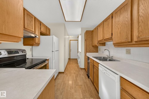 Galley kitchen featuring wood-finish cabinetry, white countertops, and a tile backsplash - #23 500 Lessard Dr Nw, Edmonton, AB 