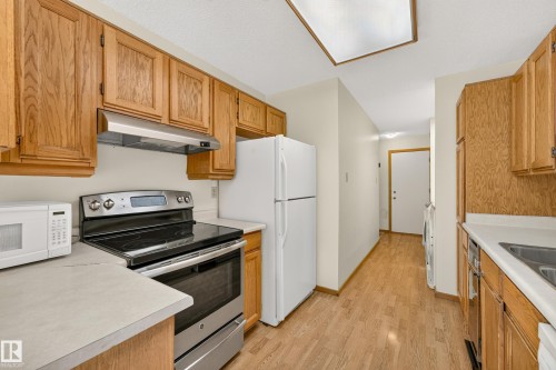 Galley kitchen with wood-finish cabinetry, stainless steel range, and light-toned countertops - #23 500 Lessard Dr Nw, Edmonton, AB 
