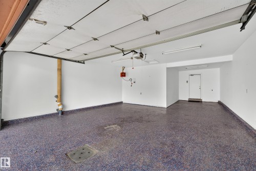 Spacious garage featuring a durable epoxy floor, white walls, overhead fluorescent lighting, and a roll-up garage door - #23 500 Lessard Dr Nw, Edmonton, AB 