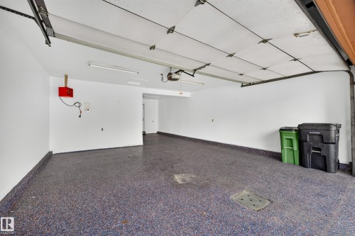 Spacious garage with an epoxy floor, overhead lighting, and white walls - #23 500 Lessard Dr Nw, Edmonton, AB 
