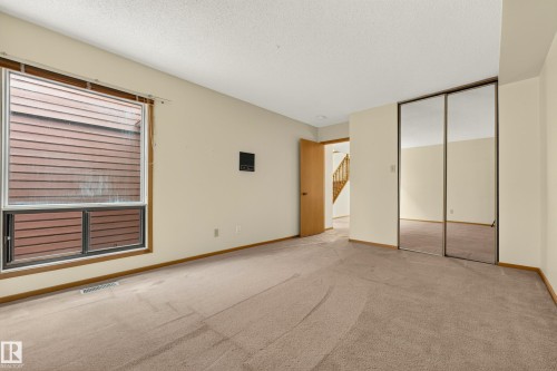 Spacious room featuring carpeting, a large window, a hollow-core door, and mirrored sliding closet doors - #23 500 Lessard Dr Nw, Edmonton, AB 