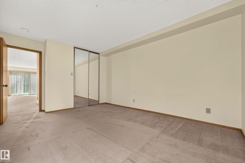 Carpeted flooring with painted walls, a wood-finish door frame, and mirrored closet doors - #23 500 Lessard Dr Nw, Edmonton, AB 