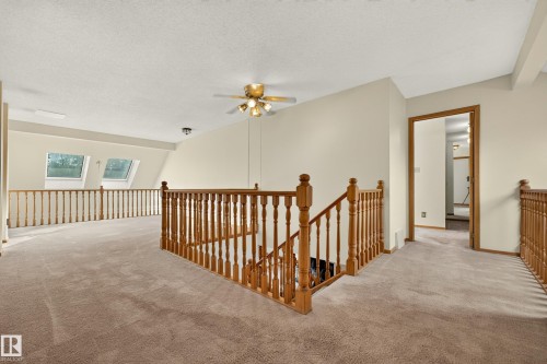 Carpeted loft area featuring wood balusters, a ceiling fan, and two skylight windows - #23 500 Lessard Dr Nw, Edmonton, AB 