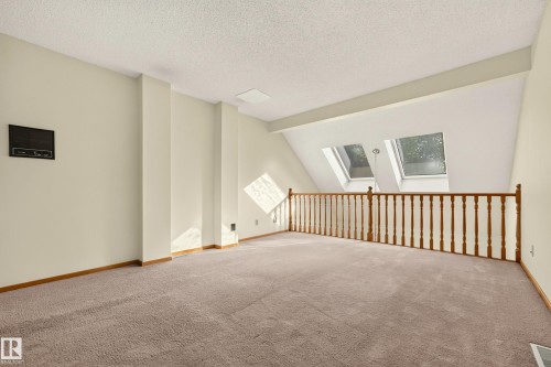 Carpeted loft area featuring a wood baluster railing, two skylight windows, and a built-in wall unit - #23 500 Lessard Dr Nw, Edmonton, AB 