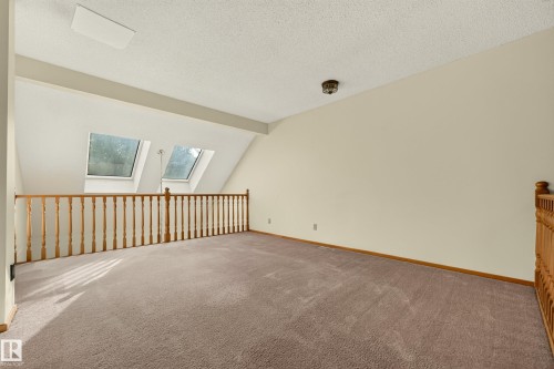 Two skylight windows illuminate this carpeted loft space, featuring a wood-finish railing and a textured ceiling - #23 500 Lessard Dr Nw, Edmonton, AB 