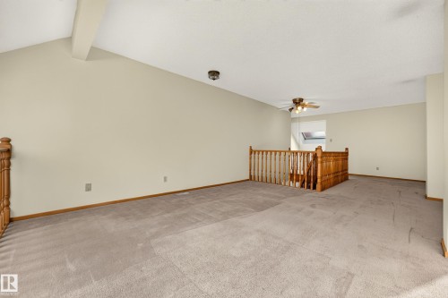 Spacious carpeted area featuring a vaulted ceiling, wood-finish railing, and ceiling fan - #23 500 Lessard Dr Nw, Edmonton, AB 
