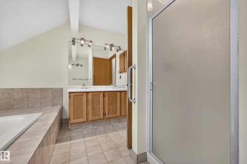 Vaulted ceiling with exposed beam, ceramic tile flooring, dual basin vanity with wood cabinetry, full-width mirror, and enclosed shower - #23 500 Lessard Dr Nw, Edmonton, AB 