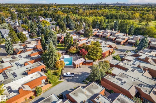 Community featuring an outdoor swimming pool, mature trees, and a distant cityscape - #23 500 Lessard Dr Nw, Edmonton, AB 