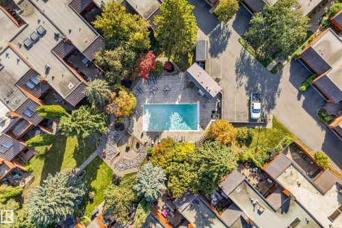 Rectangular swimming pool surrounded by established trees, paved pathways, and multiple buildings with flat roofs - #23 500 Lessard Dr Nw, Edmonton, AB 