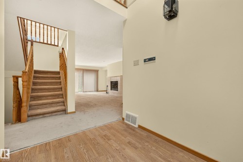 Wood-finish flooring entry leading to carpeted stairs with wood banister and an open living area featuring a fireplace with tile surround - #23 500 Lessard Dr Nw, Edmonton, AB 