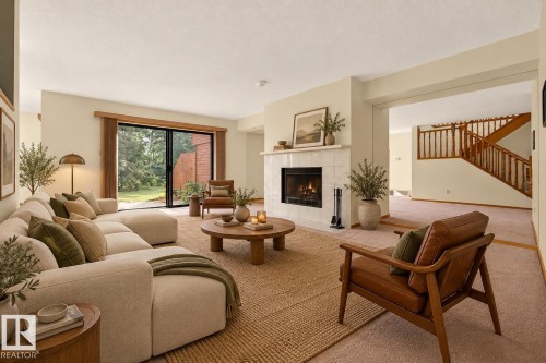 Living area featuring a tiled fireplace, wood-framed sliding glass door, and a staircase with wood banisters - #23 500 Lessard Dr Nw, Edmonton, AB 
