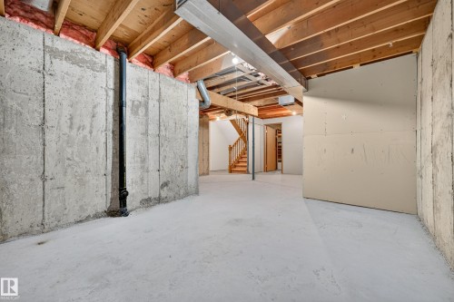 Unfinished basement featuring concrete walls and flooring, exposed wood ceiling joists, and a wood staircase - #23 500 Lessard Dr Nw, Edmonton, AB 