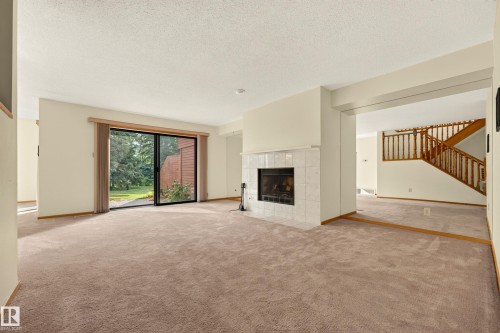 Living area featuring a tiled fireplace, sliding glass door, and carpet flooring - #23 500 Lessard Dr Nw, Edmonton, AB 