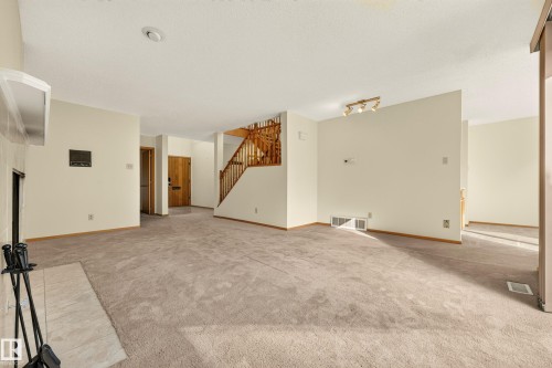 Spacious room with plush carpeting, a fireplace with a light-colored tile surround, and a wood staircase - #23 500 Lessard Dr Nw, Edmonton, AB 