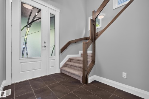 Entryway featuring double doors with decorative glass panels, dark tiled flooring, a carpeted staircase with wood railing, and a window - 11167 62 Avenue Nw, Edmonton, AB 
