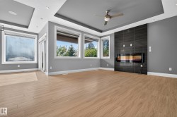 Recessed lighting with layered ceiling details, wood-finish flooring, multiple windows, built-in linear fireplace, and a ceiling fan - 