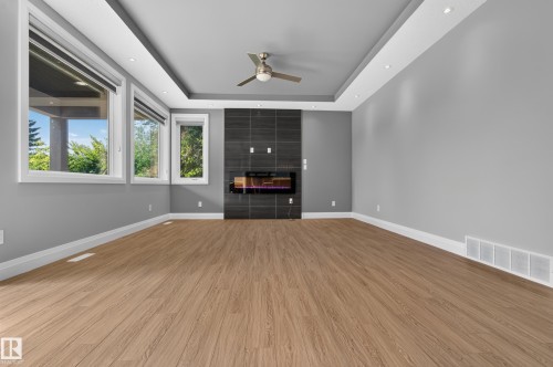 Recessed ceiling with integrated lighting, modern fireplace with dark tile surround, wood-finish flooring, ceiling fan, and multiple windows - 11167 62 Avenue Nw, Edmonton, AB 