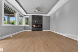 Recessed ceiling with integrated lighting, modern fireplace with dark tile surround, wood-finish flooring, ceiling fan, and multiple windows - 
